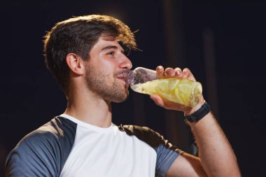 Genç bir adam, narenciye ile doldurulmuş temiz bir şişeden bir yudum alır. Geceleri dışarıda durup egzersiz yaptıktan sonra rahatlamış ve dinlenmiş görünür..