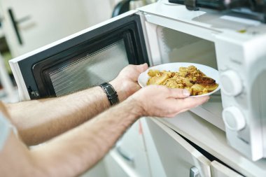 Çağdaş bir mutfakta, bir tabak güveç artıklarını mikrodalgaya koyuyor. Parlak ışıklandırma, yiyeceklerin yeniden ısıtılması için hazırlanırken temiz ve düzenli alanı geliştirir..