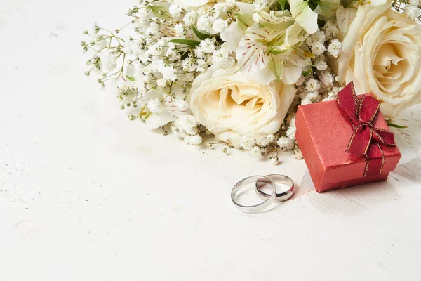 stock image Two rings, red gift box, bouquet of white flowers on white wooden background. Placed in the upper right corner of the photo.