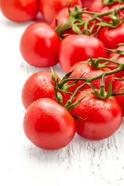 Beyaz ahşap yüzeyinde su damlaları olan olgun kiraz domatesleri. Vişneli domateslere yakın çekim. Fotoğrafın dikey yönelimi