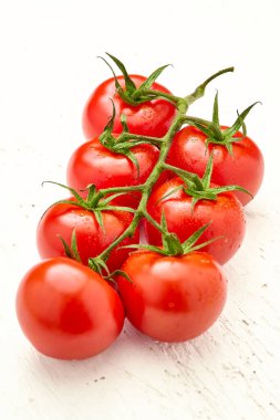 Beyaz ahşap yüzeyinde su damlaları olan olgun kiraz domatesleri. Vişneli domateslere yakın çekim. Fotoğrafın dikey yönelimi