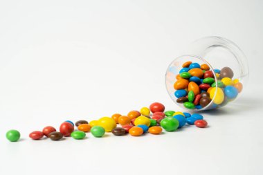 Beyaz arka planda renkli şekerler. Tatlı renkli şeker süprüntüsü. Bardakta sürükleyici