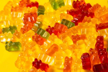 Sarı arka planda izole edilmiş renkli jelibon ayıcıkları. Tatlı marmelatlı ayılar. Sarı masada nefis parlak jöle ayılar