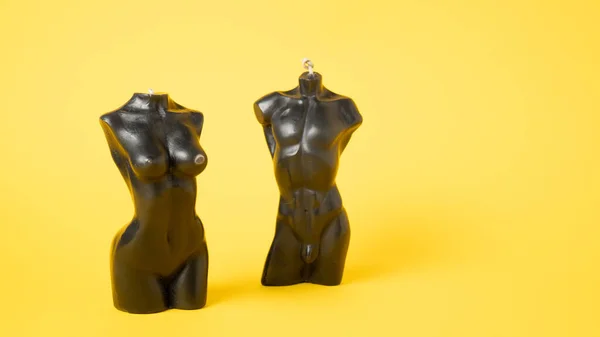 Candles in the shape of a mans and a womans bodies. Woman torso candle. Man torso candle on yellow background.