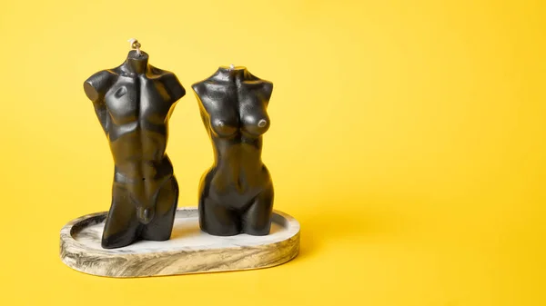 Candles in the shape of a mans and a womans bodies. Woman torso candle. Man torso candle on yellow background.