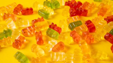 Sarı arka planda izole edilmiş renkli jelibon ayıcıkları. Tatlı marmelatlı ayılar. Sarı masada nefis parlak jöle ayılar