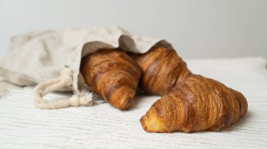 Croissants in eco bag on wooden table. Eco-friendly linen bag with fresh croissants. clipart