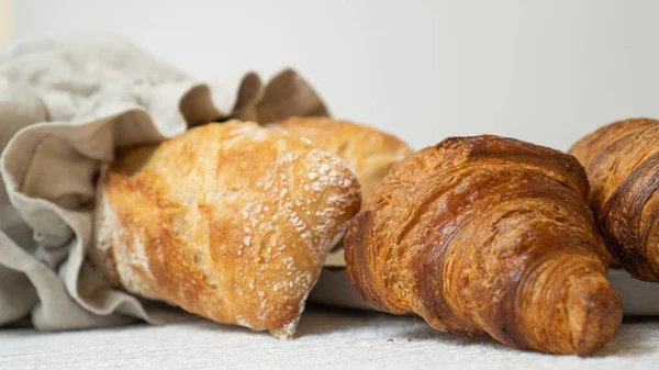 An assortment of freshly baked croissants and a rustic ciabatta in a linen bread bag, beautifully arranged on a table with an elegant tablecloth.