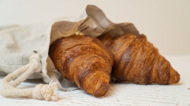 Kırsal masadaki gri çantalı kruvasanlar. Sürdürülebilir keten çantada taze pişmiş kruvasanlar..