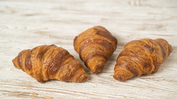 stock image Three fresh croissants on white rustic table. Homemade golden croissants on brown wooden table.