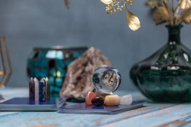 Yıpranmış ahşap bir masanın üzerinde renkli şifa kristalleri içeren bir tarot kartı okuyucusu mistisizm hissi uyandırıyor.