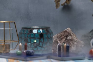 Şifalı kristaller, bir mum feneri ve yıpranmış ahşap bir yüzey üzerinde bir jeot içeren huzurlu bir tarot kartı okuma alanı.