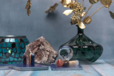 Şifalı kristaller, bir mum feneri ve yıpranmış ahşap bir yüzey üzerinde bir jeot içeren huzurlu bir tarot kartı okuma alanı.
