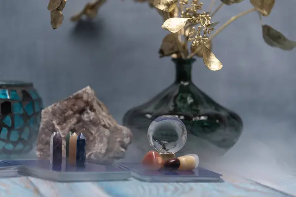 A serene tarot card reading space with assorted healing crystals, a candle lantern, and a geode on a weathered wooden surface