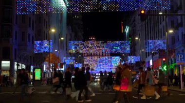 Madrid 'in Gran Via' sından alışveriş çantası taşıyan birkaç kişi, tatil sezonunda Noel ışıklarıyla süslenmiş.
