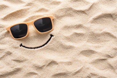 A playful smiley face drawn in the sand with sunglasses, evoking a sense of summer fun and relaxation on a sunny beach day. clipart