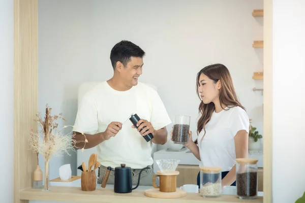 Couple or asian people to make, learn to ground coffee beans or brew coffee in kitchen home by grinder machine. Include cup, mug and kitchenware. Concept for lifestyle, love, happy, family, relationsh