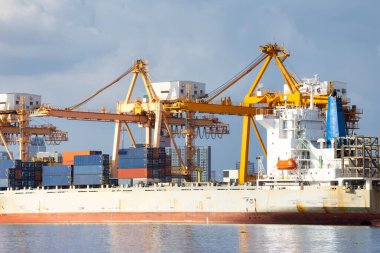 Cargo ship at dock, port or harbor. To loading cargo container, work with crane. Concept of business and industry i.e. shipping, logistics, international trade, freight transport and import export.