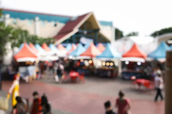 Blurred image of food fair, flea market or food festival consist of booth, tent, vendor and food stall. Busy with asian people along walking street. Event in Chiang Mai at twilight for background.