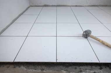 Döşeme döşemesi iç tarafta yapım aşamasında. Tokmak, beton harç çimento ve beyaz kare seramik fayans dahil. Banyo, mutfak ve duş odasında dekor yüzeyi için tamamlayıcı malzeme.