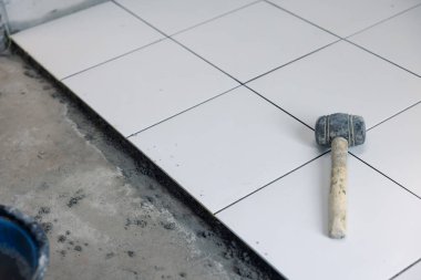 Döşeme döşemesi iç tarafta yapım aşamasında. Tokmak, beton harç çimento ve beyaz kare seramik fayans dahil. Banyo, mutfak ve duş odasında dekor yüzeyi için tamamlayıcı malzeme.