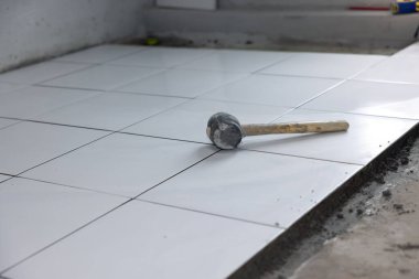 Döşeme döşemesi iç tarafta yapım aşamasında. Tokmak, beton harç çimento ve beyaz kare seramik fayans dahil. Banyo, mutfak ve duş odasında dekor yüzeyi için tamamlayıcı malzeme.