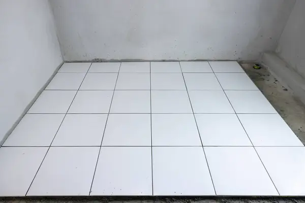 stock image Tile floor under construction in perspective view by white square ceramic tile. Finishing material for interior, decoration, installation on concrete surface floor in bathroom, kitchen and shower room