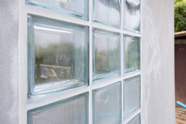 İnşaat halindeki beton duvara bakış açısıyla şeffaf cam bloğu kapat. Sınırın kenarına dolgu macunu sür. Işık için inşaat malzemesi içeri girer..