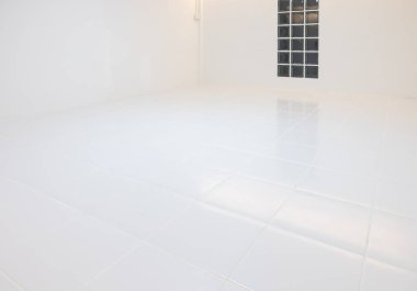 Geceleri, kare beyaz fayans döşeme desenli boş bir oda. Cam blok duvarı da dahil. Arka plan için sıcak beyaz ışıklandırmalı temiz parlak yüzey yansıması.