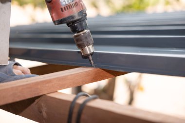 İşçi ya da müteahhit tarafından çalıştırılan ahşap kaplama. Ahırdaki gri metal levhayı ya da ahşap çerçeve yapısını tamir etmek için auger elektrikli alet kullanıyor. Çatı yapım aşamasında.