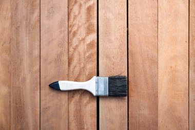 Kereste yığını üzerine boya fırçası, ahşap ürün en üstte. Yapı malzemesi ve malzeme geliştirme, koruyucu veya kaplama leke yüzeyi. Arkaplan için boş uzay giysisi ekle.