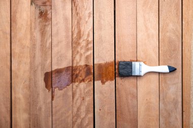 Boya fırçası kereste yığınına vernik uygular, ahşap ürünler üst görüntüde. İnşaat konsepti için ıslak ve koyu kahverengi görünün, koruyucu veya kaplama leke yüzey giysisi.