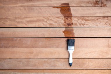 Boya fırçası kereste yığınına vernik uygular, ahşap ürünler üst görüntüde. Islak ve koyu kahverengi renkte görünün, koruyucu ya da kaplama lekeli tahıl yüzeyini geliştirin. Arkaplan için boş uzay giysisi ekle.