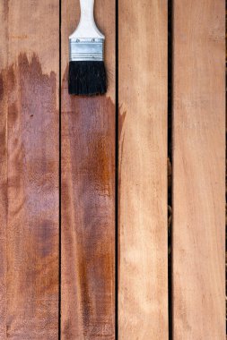 Boya fırçası yeni kereste yüzeyine vernik uygular, ahşap ürünler üst görüntüde. Yapı konsepti için ıslak, zarif ve koyu kahverengi renkli görünün..