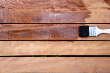 Boya fırçası yeni kereste yüzeyine vernik uygular, ahşap ürünler üst görüntüde. Yapı konsepti için ıslak, zarif ve koyu kahverengi renkli görünün..