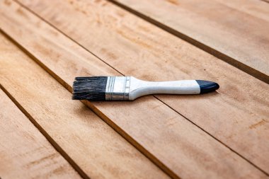 Kereste yığını üzerine boya fırçası, ahşap ürün. Yapı malzemesi ve malzeme geliştirme, koruyucu veya kaplama leke yüzeyi. Arkaplan için boş uzay giysisi ekle.