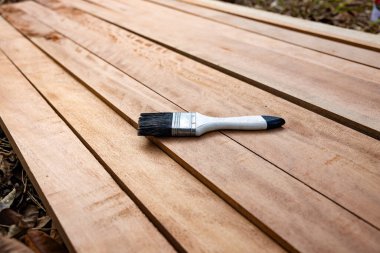 Kereste yığını üzerine boya fırçası, ahşap ürün en üstte. Yapı malzemesi ve malzeme geliştirme, koruyucu veya kaplama leke yüzeyi. Arkaplan için boş uzay giysisi ekle.