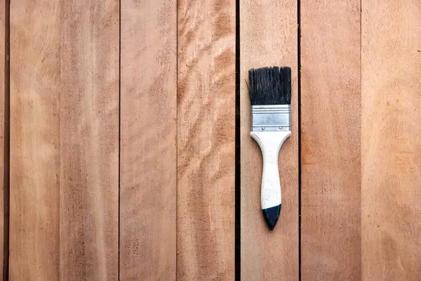 Kereste yığını üzerine boya fırçası, ahşap ürün en üstte. Yapı malzemesi ve malzeme geliştirme, koruyucu veya kaplama leke yüzeyi. Arkaplan için boş uzay giysisi ekle.