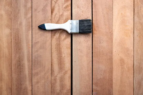 Kereste yığını üzerine boya fırçası, ahşap ürün en üstte. Yapı malzemesi ve malzeme geliştirme, koruyucu veya kaplama leke yüzeyi. Arkaplan için boş uzay giysisi ekle.