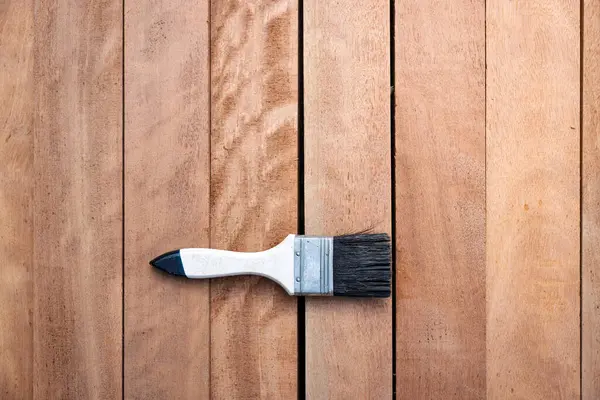 Kereste yığını üzerine boya fırçası, ahşap ürün en üstte. Yapı malzemesi ve malzeme geliştirme, koruyucu veya kaplama leke yüzeyi. Arkaplan için boş uzay giysisi ekle.