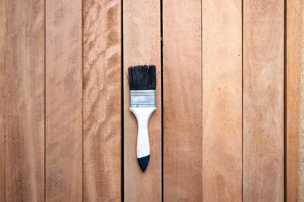 Kereste yığını üzerine boya fırçası, ahşap ürün en üstte. Yapı malzemesi ve malzeme geliştirme, koruyucu veya kaplama leke yüzeyi. Arkaplan için boş uzay giysisi ekle.