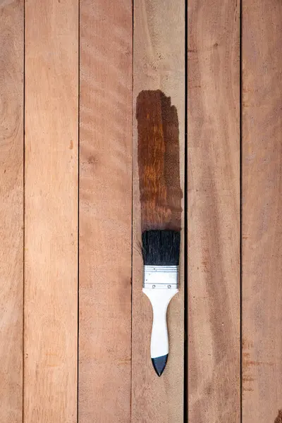 Boya fırçası kereste yığınına vernik uygular, ahşap ürünler üst görüntüde. Islak ve koyu kahverengi renkte görünün, koruyucu ya da kaplama lekeli tahıl yüzeyini geliştirin. Arkaplan için boş uzay giysisi ekle.