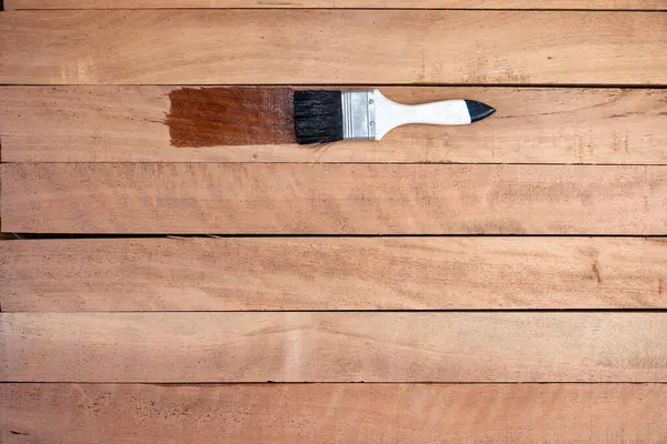 Boya fırçası, kereste yığınına vernik kimyasal ürün uygular. Parlak ve koyu kahverengi renkte görünün. Geliştirmek, korumak ya da lekelemek için. Arkaplan için boş uzay giysisi ekle.