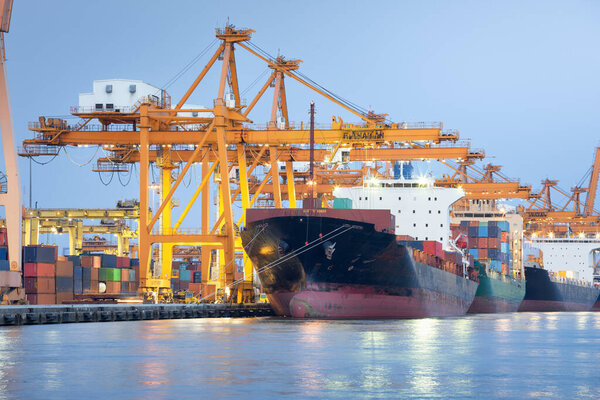 Gantry crane or crane port working with cargo container on large cargo ship at front view in twilight. Beside jaopraya river, Bangkok of Thailand. Concept of transport, global trade and import export.