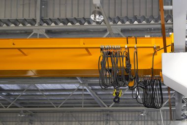 Fabrikada ya da depoda vinç var. Üretim ve kargo taşımacılığı için kiriş yapının üzerinde vinç, kanca ve tel halat ile endüstriyel makine veya kaldırma ekipmanları.