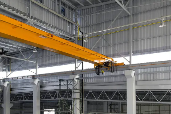 Fabrikada ya da depoda vinç var. Üretim ve kargo taşımacılığı için kiriş yapının üzerinde vinç, kanca ve tel halat ile endüstriyel makine veya kaldırma ekipmanları.