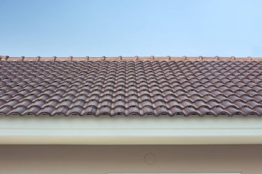 Mavi gökyüzü arkaplanlı ev binasını kaplayan çatı fayanslarının manzarası. Kırmızımsı kahverengi renkli terracotta materyali. Birbirine kenetlenmiş model tasarımı, modern mimari tarzı..