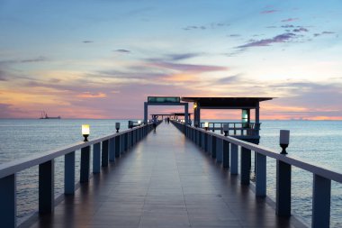 Uzun iskele zemini, karanlık alacakaranlık gökyüzünün altında, alacakaranlığın parlak akımına karşı siluetiyle ufka doğru uzanıyor. Sükunet ve rahatlığı temsil eden sahne deniz manzarası arkaplanı.
