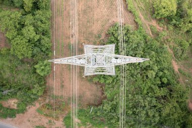 Overhead power transmission tower, steel lattice structure rising above vibrant green landscape. Represents electricity infrastructure, high-voltage energy distribution and rural development.