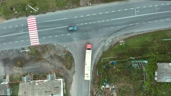 一辆运送人道主义援助物资的卡车穿过一座被摧毁的城市 以躲避俄国对乌克兰的侵略 红色卡车 蓝色和黄色拖车 摧毁了城市和道路 4K空中 — 图库照片